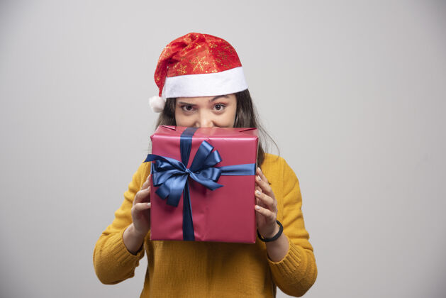 圣诞老人戴圣诞帽的快乐女人躲在礼品盒后面人欢呼微笑