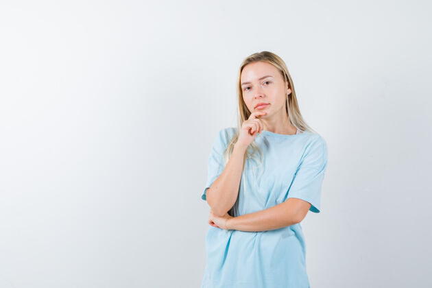 微笑金发女孩用手托着下巴 穿着蓝色t恤 站在思考的姿势里 面带沉思时尚女孩健康