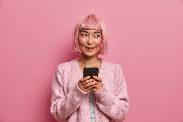 发型科技 通讯和生活方式的概念令人高兴的梦幻女子染成玫瑰色的头发 手持手机 使用现代应用程序与朋友信息 粉色头发手机室内