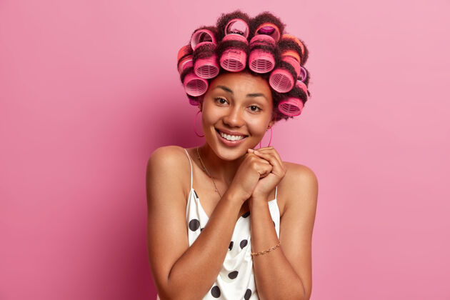 美丽积极迷人的黑皮肤成年非裔美国妇女应用卷发器 有温柔的微笑 穿着休闲装 摆姿势牙齿漂亮理发师