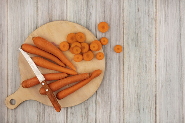 胡萝卜顶视图减肥友好的食物胡萝卜在一个木制的厨房板与刀切碎的胡萝卜在一个灰色的木制墙壁复制空间板饮食视图