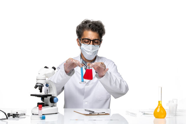 专业正面图穿着特殊套装的中年科学家坐着拿着装有解决方案的烧瓶坐着研究实验室
