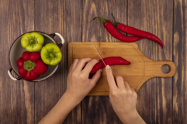 新鲜俯视图中的女性手切辣椒在木制厨房板上用刀在木墙上板顶部烹饪