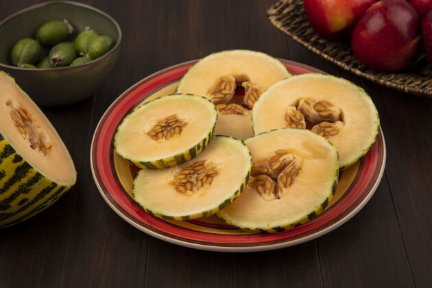 哈密瓜甜瓜片放在盘子里的俯视图 苹果放在木制墙上的柳条托盘上观点柳条瓜
