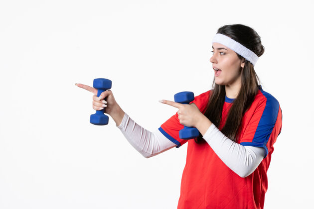 视图正面图穿着运动服的年轻女性在白墙上用哑铃锻炼健身房白色运动