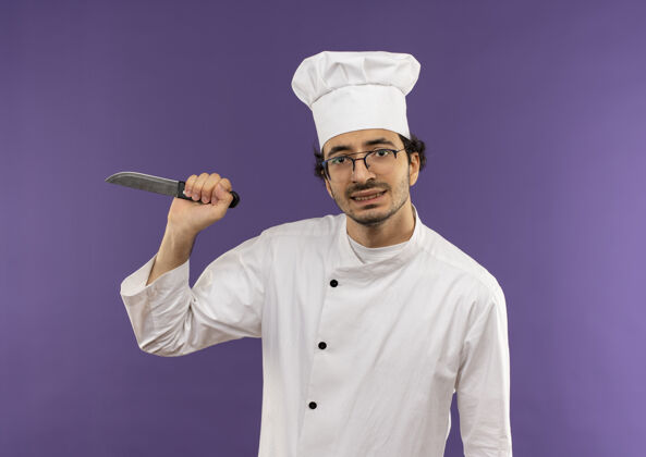 持有紧张的年轻男厨师穿着厨师制服 戴着眼镜 手持紫色的刀刀紫色眼镜