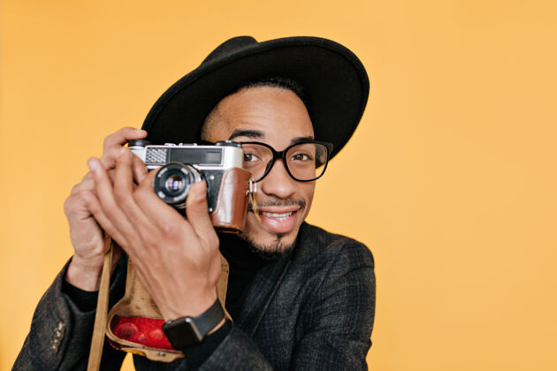 深色头发棕色眼睛和深色皮肤的男性摄影师的特写照片微笑着的非洲男人用相机工作放松表情室内