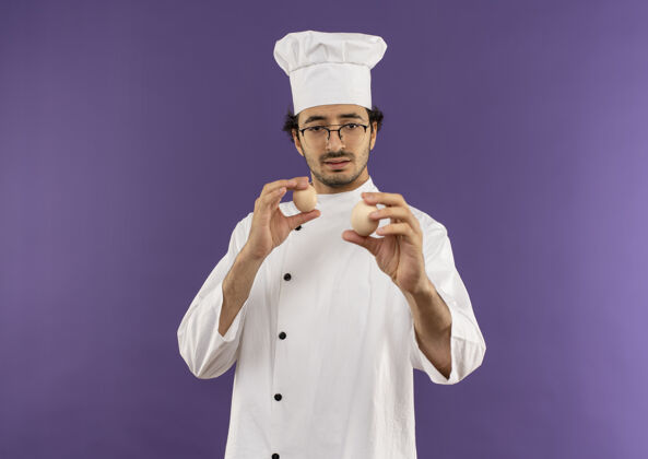 持有想着年轻的男厨师穿着厨师制服 戴着眼镜拿着紫色的鸡蛋看着厨师紫色年轻