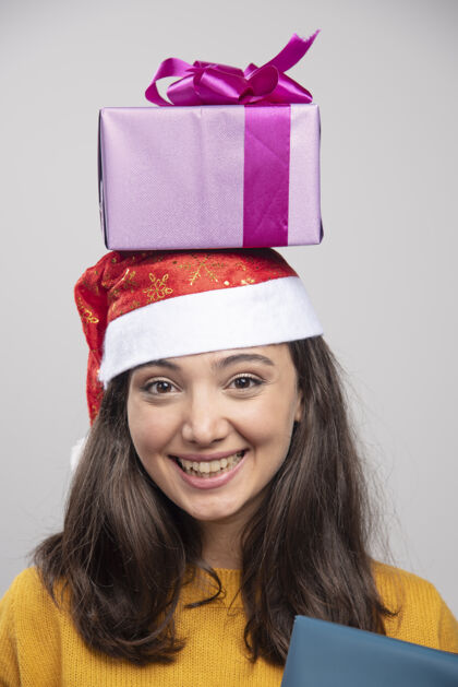 冬天戴圣诞帽的年轻女子头顶上拿着礼品盒欢呼年轻黑发