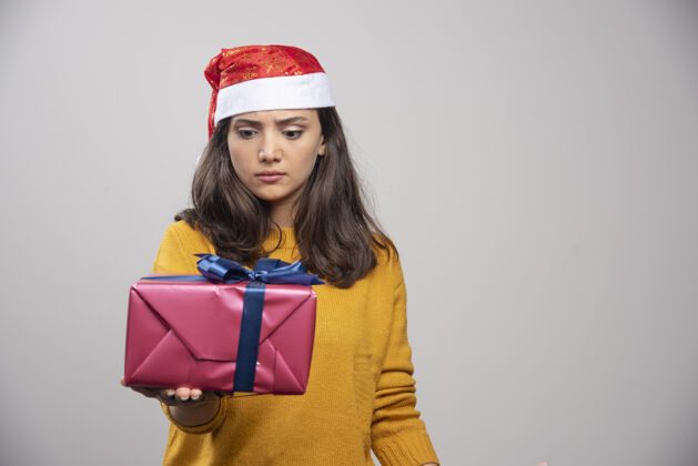 圣诞节戴圣诞帽的年轻女子在看一个礼品盒人肖像乐趣