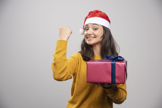 惊喜戴着圣诞帽的黑发女人伸出拳头 手里拿着礼盒黑发快乐漂亮