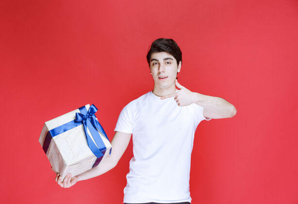 成人男人拿着一个白色的礼盒 并显示积极的手势年轻姿势模特