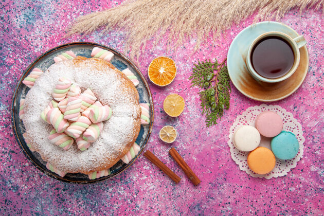 含糖粉红色表面上有一杯茶和麦卡龙的糖粉蛋糕俯视图美味顶视图新鲜