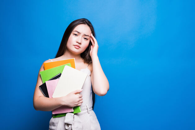 成人美丽的亚洲年轻女子在蓝色的墙上看书亚洲学习微笑