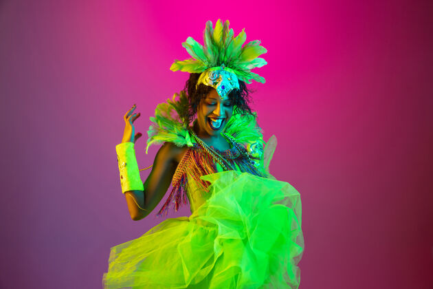 羽毛美丽的年轻女子在嘉年华 时尚的化装服装与羽毛跳舞的梯度背景在霓虹灯下人类黄金节日