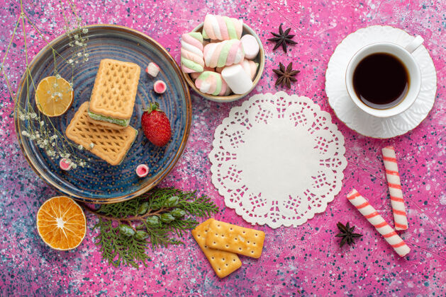 鲜花浅粉色表面上有一杯茶和棉花糖的美味华夫饼俯视图茶顶视图棉花糖