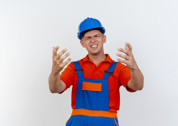 头盔年轻的男建筑工人穿着制服 戴着安全帽 两眼紧闭 手伸向白色的摄像机眼睛年轻关注