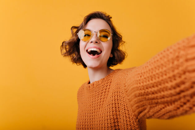 漂亮戴着滑稽黄色太阳镜的笑艳女人自拍穿着针织毛衣的放松的白人女孩自拍的肖像女人微笑快乐
