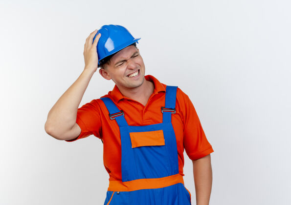 建筑工人年轻的男建筑工人穿着制服 戴着安全帽 手放在头上 戴着白色的帽子眼封闭男性