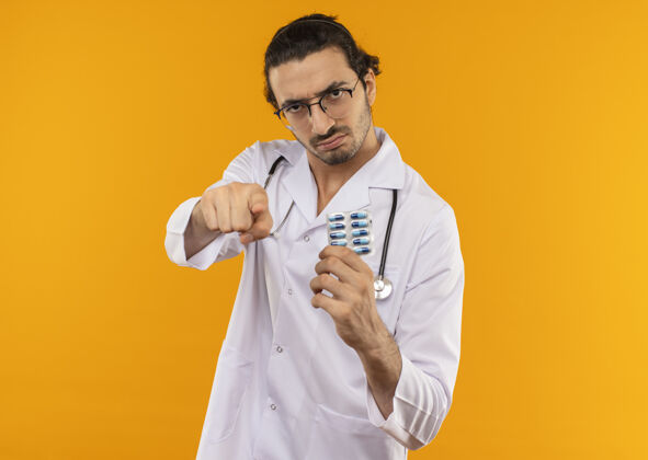 年轻年轻的医生戴着医用眼镜 穿着医用长袍 手持听诊器 拿着药片 在黄色屏幕上给你看手势医学手势复制