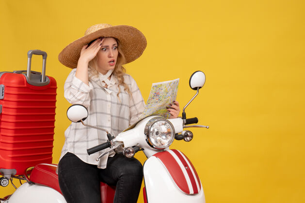 衣服俯视图中惊讶的年轻女子戴着帽子 坐在摩托车上 专注于地图上的黄色比赛集中顶