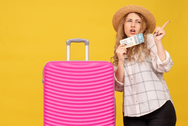 购物者顶视图年轻女士戴着帽子拿着票 站在她粉红色的包旁边指着左边的东西拿着附近包