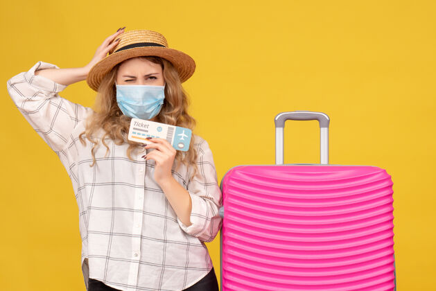 人困惑的年轻女士戴着面具 出示车票 站在黄色的粉红色袋子旁边医院近成人