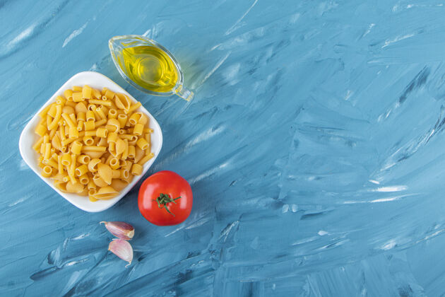 未经料理一块白板 上面是油和新鲜的红色西红柿 背景是蓝色的蔬菜番茄油
