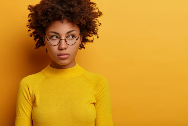 想象沉思的年轻女模特特写镜头戴着圆眼镜广告黄衣服 神情沉思地侧视 思考着计划 摆出室内 空白处为你的广告肖像思考雇员