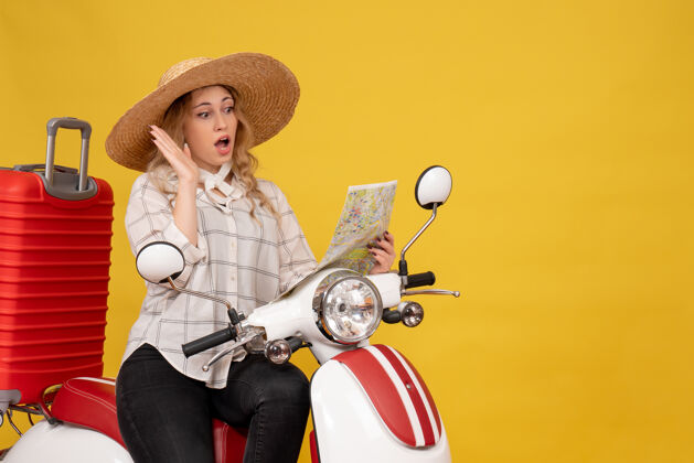 地图戴帽子坐在摩托车上看地图的年轻女子的俯视图 黄色的脸上有着令人惊讶的压抑感上衣漂亮穿着