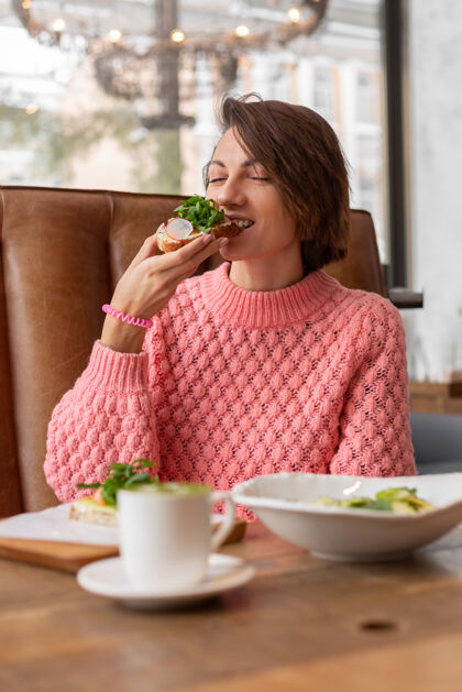 切片一个穿着舒适温暖毛衣的女人在餐厅里吃着健康的早餐烤面包 芝麻菜和三文鱼享受面包吐司