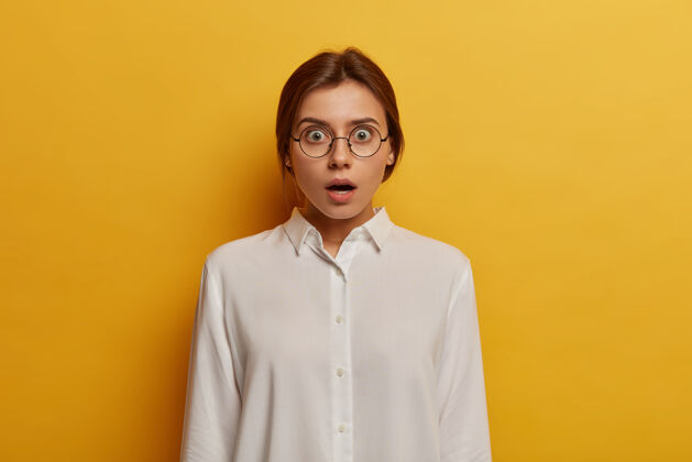 意外天哪 我不相信震惊情绪化的女人戴着大眼镜和白衬衫 对令人惊讶的消息做出反应 睁大眼睛 隔着黄色的墙人和情绪的概念干净情绪眼镜