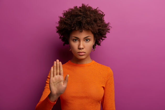 拒绝够了严肃严厉的女人做了停止的手势 表示禁止和要求坚持 拒绝的东西 穿橙色毛衣 孤立在紫色的墙壁上决不是永远 不进入它禁止表情禁止