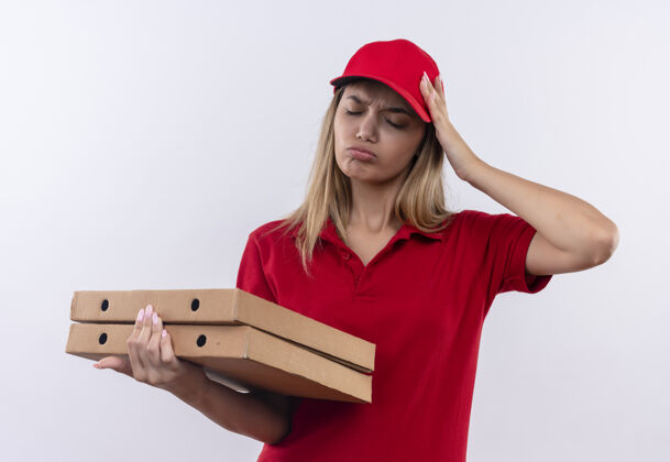 关闭闭上眼睛悲伤的年轻送货女孩穿着红色制服 戴着帽子 手里拿着披萨盒 手放在头上 与白色隔离年轻女人手势