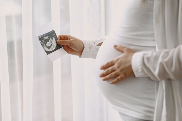 站立孕妇站在窗边看照片母亲健康婴儿