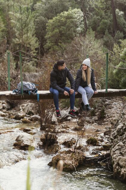 探索带着背包坐在桥上的情侣女人河流一起