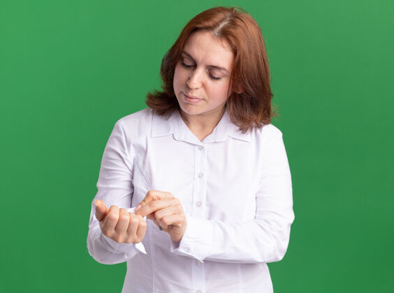 衬衫站在绿色的墙上 一个穿着白衬衫的年轻女子正在修袖扣 看上去很自信女人修复站立