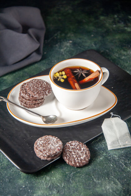 食物前视图：茶杯加巧克力饼干放在盘子里 托盘上放在深色的表面上 仪式用玻璃做甜点 甜点的颜色咖啡甜点饼干