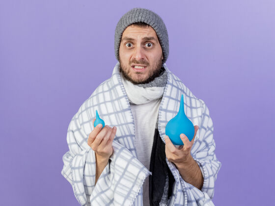 生病关心的年轻病人戴着冬天的帽子和围巾拿着灌肠隔离在紫色的背景帽子围巾灌肠
