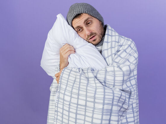 包裹望着旁边一个戴着冬天帽子 围巾裹着格子布的年轻病夫 抱着一个孤立在紫色背景上的枕头疾病壁板不愉快