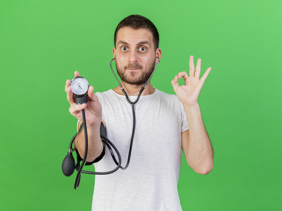 压力年轻的病人戴着听诊器 用隔离在绿色背景上的血压计测量自己的血压 这让他很高兴自己的疾病年轻