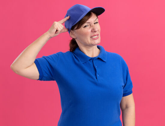 女人身穿蓝色制服 头戴帽子的中年女送货员 手放在头上 站在粉红色的墙上 看上去很困惑 很焦虑分娩站头