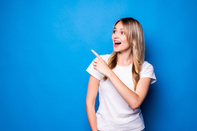 女性一个年轻的女人用手指着隔离的蓝色墙壁欢迎休闲欢呼