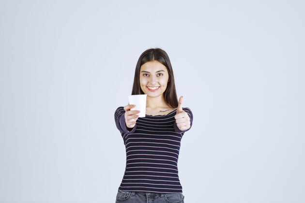 雇员穿着条纹衬衫的女孩拿着一个塑料咖啡杯 指着一个好味道人体模特成人人类