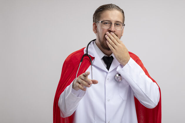 家伙一个年轻的超级英雄 穿着医用长袍 戴着听诊器 戴着眼镜 用手捂着嘴 在白色背景上显示你的手势眼镜年轻手