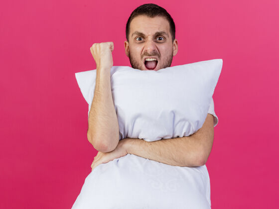 疾病快乐的年轻病人抱着枕头 在粉色背景上显示“是”的手势拥抱姿势是的