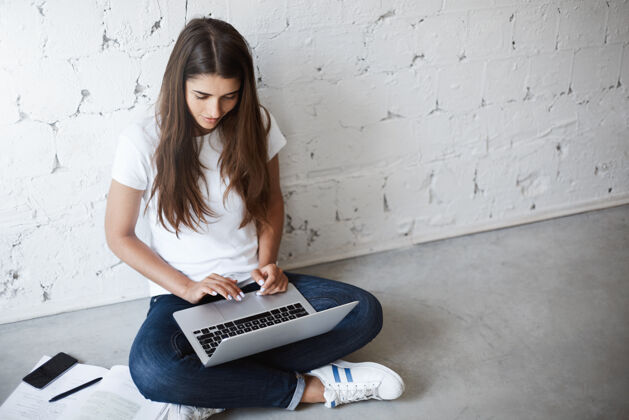 电脑创意年轻女性的俯视图 坐在地板上 靠在墙上 用笔记本电脑 周围都是小玩意和书籍设计师正在进行她明天需要展示的新项目学习概念无线学生智能