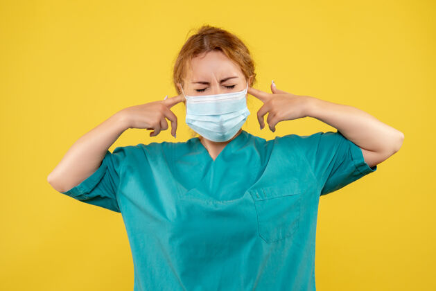 套装黄墙上年轻女医生穿着医疗服 戴着口罩的正面图医院年轻女医生面具
