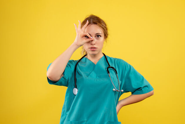 病毒黄色墙壁上穿着带听诊器的医疗服的女医生的正视图健康套装人