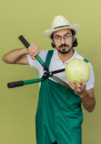 剪子自信的男园丁戴着眼镜戴着园艺帽拿着剪刀和卷心菜复制绿色帽子